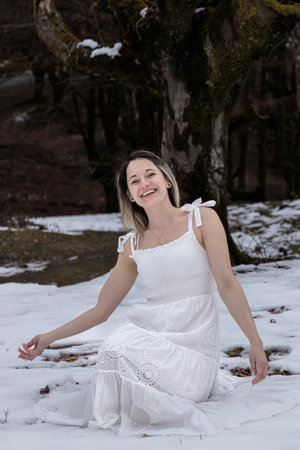 woman in a white dress sitting on a snowy ground in a forestの写真素材