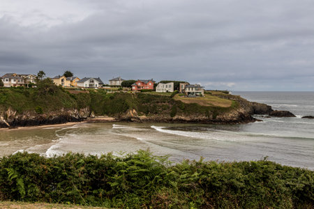 coastal town, with houses on a cliff overlooking a dark blue ocean under a cloudy skyの写真素材