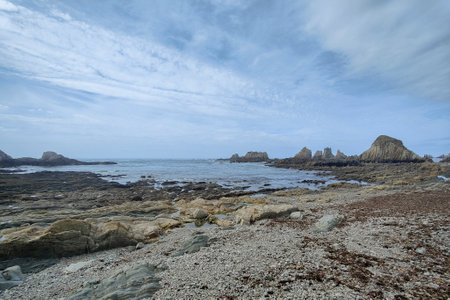 rocky beach with the deep blue ocean in the background under a light blue sky with white cloudsの写真素材