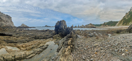 rocky beach with jagged rocks and cliffs under a blue sky with scattered cloudsの写真素材