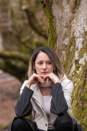 woman is sitting against a tree, their hands forming a heart shape, in a forest settingの写真素材