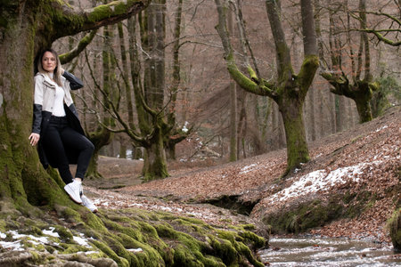 woman on a moss-covered tree branch in a forest, with a stream visible in the backgroundの写真素材