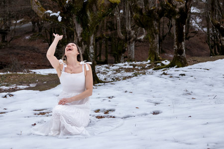 woman in a white dress is laughing joyfully while sitting in a snowy forest, creating a serene and peaceful sceneの写真素材