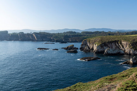 stunning coastline with towering cliffs, deep blue water, and distant mountains under a clear skyの写真素材