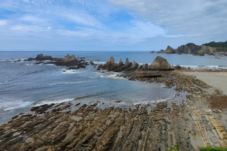 rocky beach with jagged rocks and cliffs in the background, taken on a day with a light blue skyの写真素材