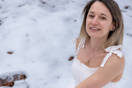 a person in a white dress standing in a snowy landscape, barefoot, with an overcast sky overheadの写真素材