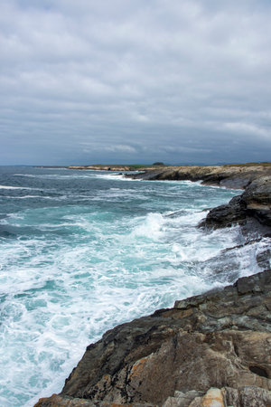 dramatic seascape: turbulent waves crash against a rocky coastline under a cloudy sky, evoking nature s raw powerの写真素材