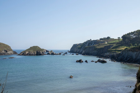 tranquil coastal scene with clear blue waters, rocky islets, lush cliffs, and a bright, inviting skyの写真素材
