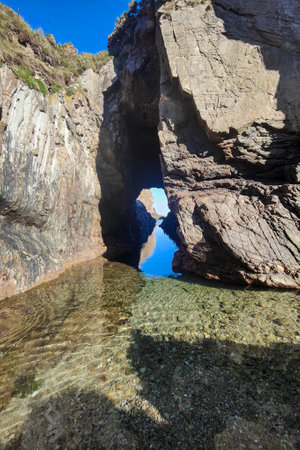 natural archway leads to a clear pool, reflecting the sky amidst rugged terrain, evoking tranquility and untouched beautyの写真素材