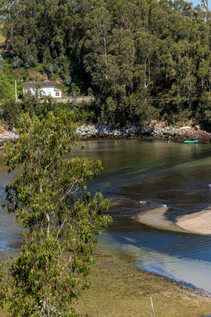 serene landscape with a house, lush greenery, secluded beach, clear waters, and a solitary boat. Tranquil and picturesqueの写真素材