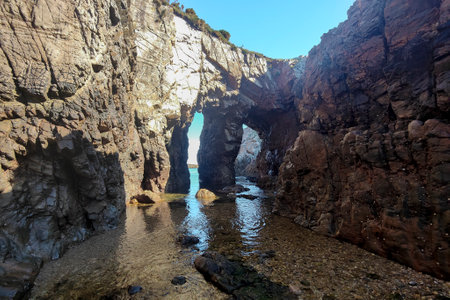 a rocky coastline with natural arches, calm waters reflecting sunlight, under a clear blue sky