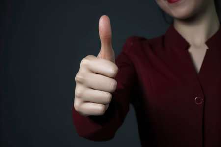 A woman in a dark red outfit gives a thumbs up, symbolizing positivity against a contrasting dark backdropの素材