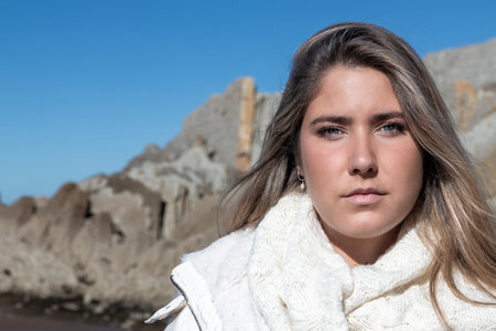 woman in a white jacket stands in front of rocky formations under a clear blue sky, exuding a sense of tranquilityの写真素材