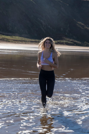 person running on a wet sandy beach, with green hills and clear skies in the backgroundの写真素材