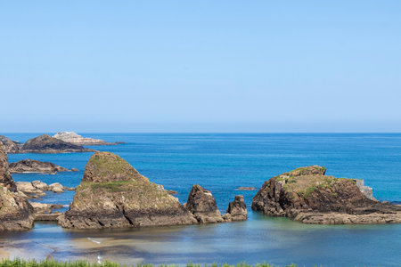 serene coastal landscape with rocky formations, clear blue sky, and calm turquoise watersの写真素材