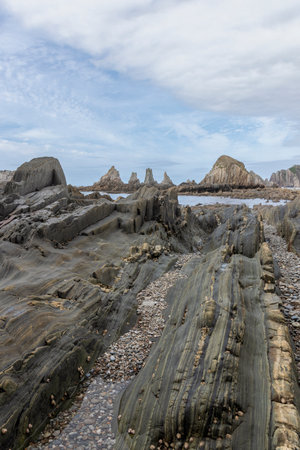 serene, rugged shoreline with distinct, eroded rock formations under a cloudy sky