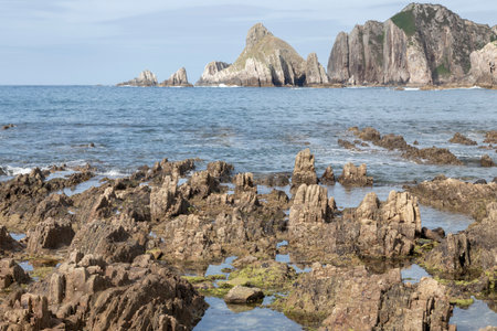 a rocky shoreline with jagged formations, pools of water, and towering cliffs in the background under a clear skyの写真素材