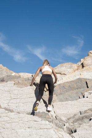 woman is climbing a mountain wearing a white tank top and black pants. Concept of determination and adventureの写真素材