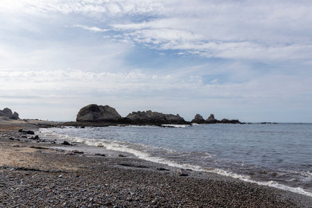 peaceful pebble beach with calm waters, large rocks, and a cloudy sky, creating a tranquil atmosphereの写真素材