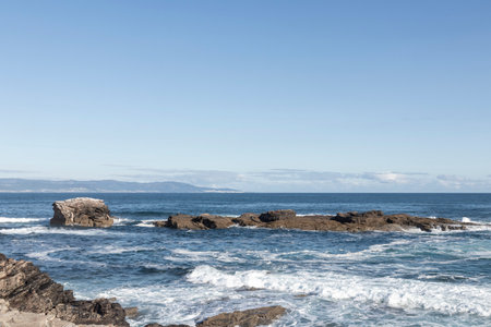 serene seascape with rocky formations, waves crashing under a clear blue sky, evoking a sense of...