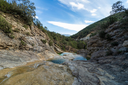 serene natural landscape with rocky terrain, clear pools of water, surrounded by lush greenery under a partly cloudy skyの写真素材