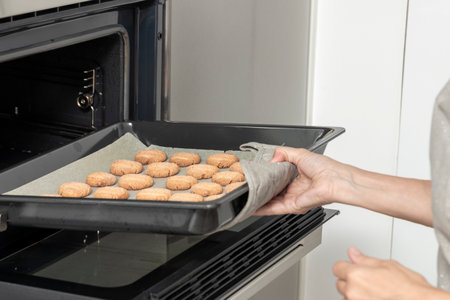 person pulling a tray of freshly baked cookies from an oven, using a cloth for safetyの写真素材