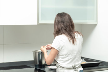 person cooking in a modern kitchen, standing at the stove with a pot and tray nearbyの写真素材