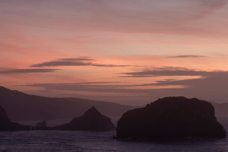 serene sunset with silhouetted mountains and rock formations against a gradient sky, evoking peace and tranquility in san juan de gaztelugatxeの写真素材