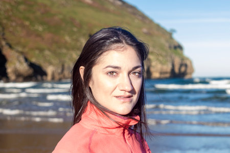 Young woman in pink jacket standing on beach with ocean and cliffs in background. portrait photography. Nature and travel conceptの写真素材