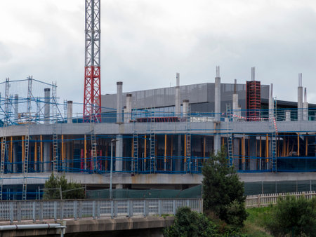 Building Under Construction with Safety Netting and Crane on a Cloudy Dayの写真素材