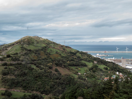 View of Green Hills Overlooking the Coastline and Wind Turbines on a Cloudy Dayの写真素材