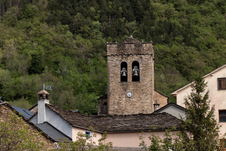 Rustic stone bell tower of a village church surrounded by lush green forested hillsの写真素材