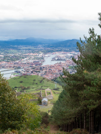 Elevated view of a city by the river, surrounded by mountains and greenery, seen through a forested path.の写真素材