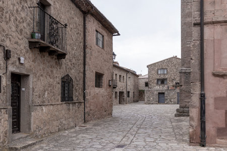 Quiet cobblestone street in a historic European village surrounded by rustic stone buildings and iron balconies.の写真素材