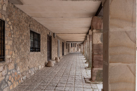 Historic stone colonnade with arched walkway and rustic architecture in a quiet village setting.の写真素材