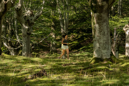 Woman jogging through a lush green forest, surrounded by tall trees and moss-covered ground. A peaceful and natural outdoor exercise settingの写真素材