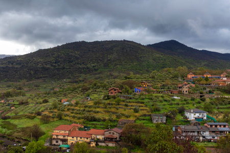 Small colorful houses and farms covering green hills under a cloudy sky in spain