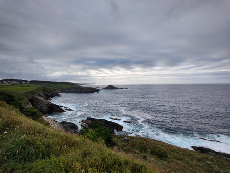 Waves crashing against a rocky coastline under a dramatic cloudy sky, creating a beautiful and powerful seascapeの写真素材