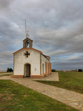 Scenic view of a small white chapel with a bell tower, located on a grassy field under a cloudy skyの写真素材
