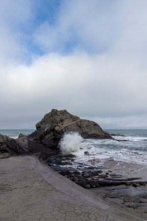 Powerful ocean waves crashing against rocks on a cloudy day, creating a dramatic scene of natural beautyの写真素材
