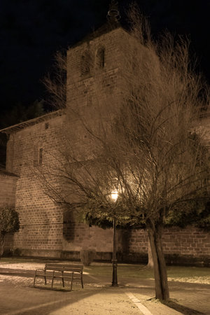 Medieval church stands majestically against the night sky, illuminated by a warm streetlamp, creating a serene and timeless sceneの写真素材