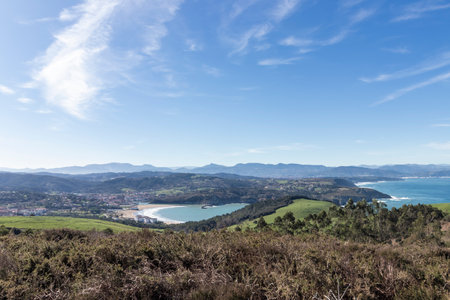 Stunning panoramic view of a picturesque bay, green hills, and distant mountains under a clear blue sky in northern spainの写真素材