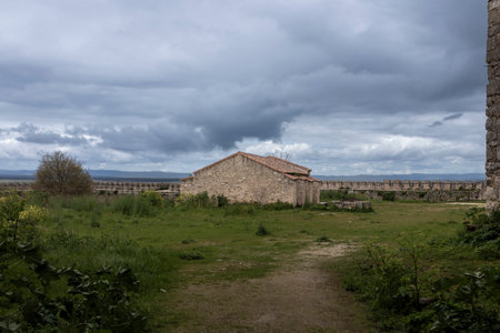 Grass field with an old stone building inside the walls of the loarre castle in aragon, spain, under a cloudy skyの写真素材