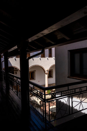 Sunlight illuminating tables in a courtyard of a historic building, seen from a dark wooden balconyの写真素材