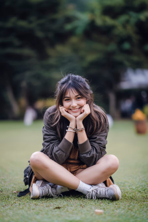 Happy young woman sitting cross-legged on grass in a park, enjoying a peaceful moment outdoorsの素材