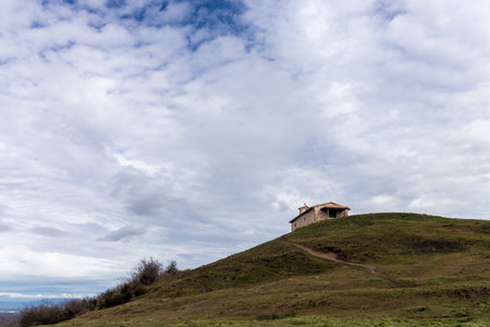 Scenic view of a small hermitage standing on top of a green hill under a cloudy sky, evoking peace and tranquilityの写真素材