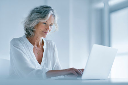 Smiling mature professional woman typing on laptop keyboard, working remotely in home officeの素材