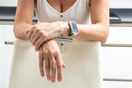 Woman wearing a smartwatch is leaning on a chair in a modern kitchenの写真素材