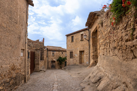 Charming cobblestone street with stone houses and blooming flowers in peratallada, a picturesque medieval village in catalonia, spainの写真素材