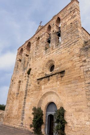 Low-angle view of the medieval church of peratallada, showcasing its weathered stone walls, bell tower, and a cloudy skyの写真素材